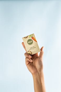A close-up of a hand holding a natural handmade soap bar against a light background.