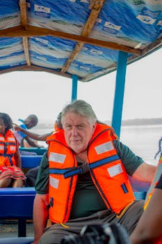 A man wearing a life vest sits in a motorboat, enjoying a scenic ride.