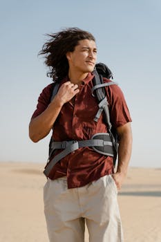 A young male traveler with long hair stands confidently in a vast desert, exuding adventure.