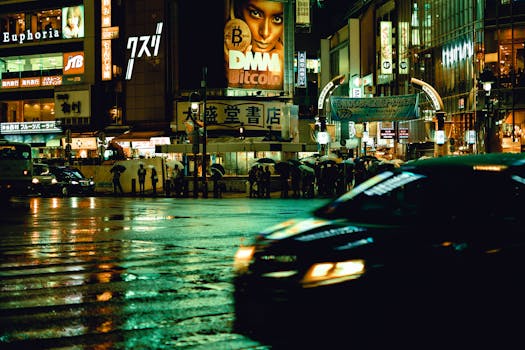 City lights reflecting on wet streets in Shibuya, Tokyo, with blurred traffic and pedestrians carrying umbrellas.
