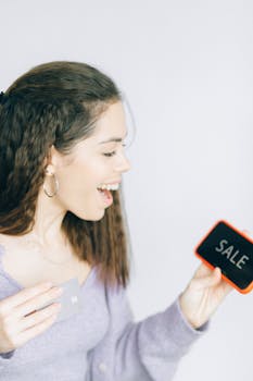 Happy woman holding a smartphone and sale sign, showcasing excitement for shopping deals.
