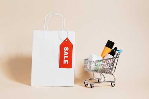 White shopping bag with red sale tag and mini shopping cart on beige background.