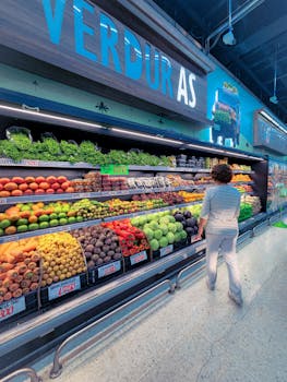 Woman browsing fresh fruits and vegetables in a supermarket aisle.